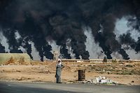 TOPSHOT - A woman stands along the side of a road on the outskirts of the town of Tal Tamr near the Syrian Kurdish town of Ras al-Ain along the border with Turkey in the northeastern Hassakeh province on October 16, 2019, with the smoke plumes of tire fires billowing in the background to decrease visibility for Turkish warplanes that are part of operation "Peace Spring". (Photo by Delil SOULEIMAN / AFP)