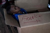 TOPSHOT - A migrant child sits in a cardboard box with the inscription "France" aboard the Ocean Viking rescue ship on November 10, 2022 in the Tyrrhenian Sea between Italy and Corsica island. - France said on November 10, 2022 that it would allow a rescue ship carrying more than 200 migrants to dock on its southern coast and disembark its passengers, harshly criticising Italy for failing to take them in. (Photo by Vincenzo Circosta / AFP)