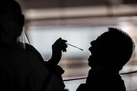 A taxi driver (R) gets tested by health workers (L) for coronavirus COVID-19 at a makeshift testing station in a carpark in Hong Kong on July 19, 2020. - The deadly coronavirus is spreading out of control in Hong Kong with a record 100 new cases confirmed, the finance hub's leader said as she tightened social distancing measures to tackle the sudden surge in infections. (Photo by ISAAC LAWRENCE / AFP)