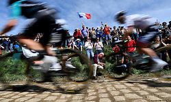 (FILES) In this file photo taken on April 8, 2018 spectators watch cyclists as they drive across cobbled stone during the 116th edition of the Paris-Roubaix one-day classic cycling race, between Compiegne and Roubaix, in Quievy, northern France. - The International Cycling Union (UCI) announced on April 1, 2021, that Paris-Roubaix, the "queen of classics", cycle race has been postponed from April 11 to October 3 because of the ongoing coronavirus (Covid-19) pandemic. (Photo by JEFF PACHOUD / AFP)