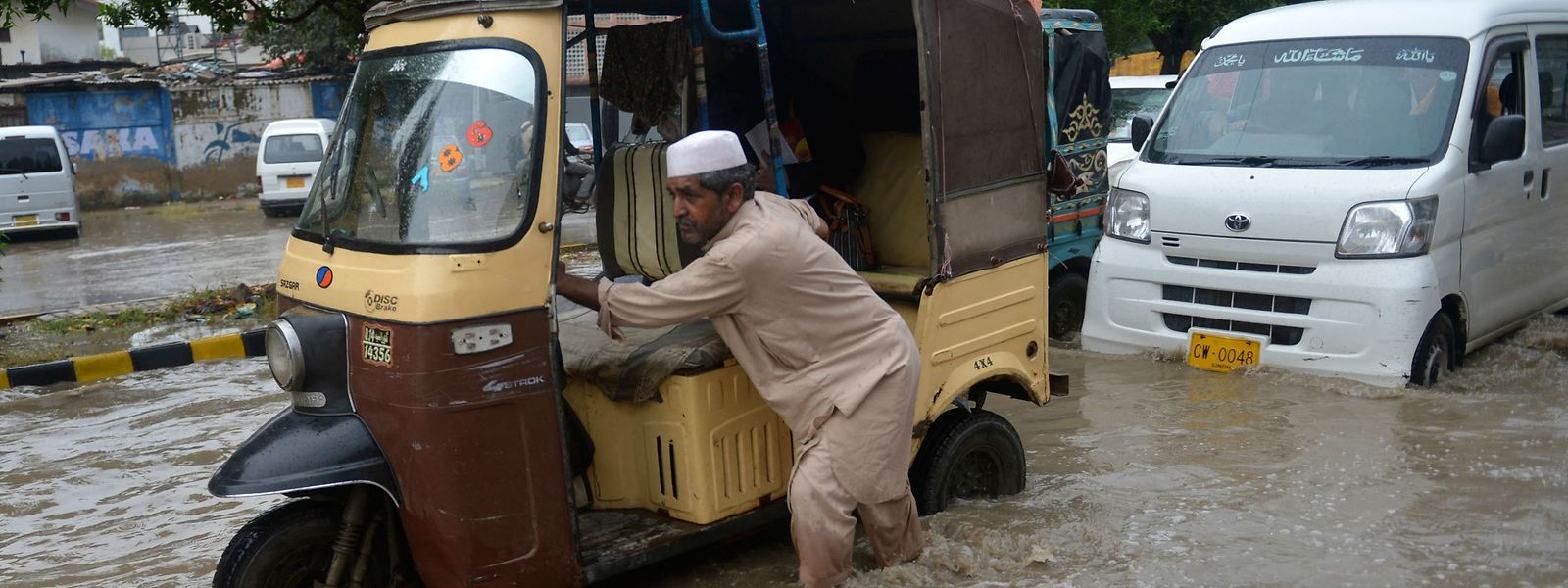 Um homem empurra o seu veículo numa rua inundada após fortes chuvas em Karachi, esta terça-feira