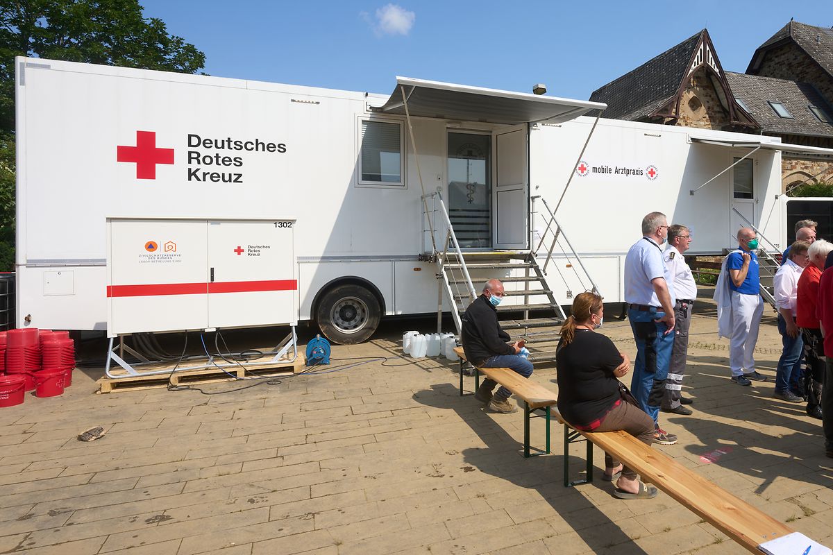 In Bad Neuenahr-Ahrweiler warten Menschen vor einer mobilen Arztpraxis des Deutschen Roten Kreuzes (DRK).