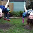 Young sisters having fun and hanging upside down on their swings in a UK garden in the Spring.
