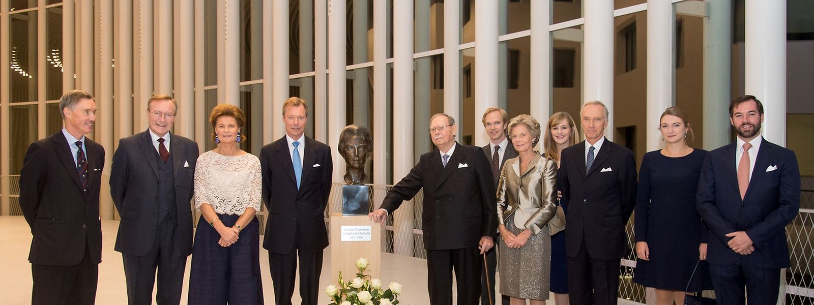 Die großherzogliche Familie posiert neben der Büste von Großherzogin Joséphine-Charlotte. Von links nach rechts: Prinz Guillaume, Prinz Jean, Prinzessin Margaretha, Großherzog Henri, Großherzog Jean, Erzherzogin Marie-Astrid, Erzherzog Christian, Erbgroßherzogin Stéphanie und Erbgroßherzog Guillaume. In zweiter Reihe: Erzherzog Imre und Erzherzogin Kathleen.