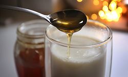 ILLUSTRATION - 20.12.2019, Bayern, Kaufbeuren: Honig fließt von einem Löffel in ein Glas mit heisser Milch. Jeder kennt irgendein Hausmittel, dass bei Erkältung Abhilfe schafft - angeblich. Denn viel Forschung zu Hausmitteln gibt es nicht. (zu dpa "Erkältungszeit: Hausmittel sind oft eine Wohltat, aber kaum erforscht") Foto: Karl-Josef Hildenbrand/dpa +++ dpa-Bildfunk +++