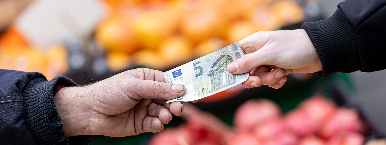 Ein Kunde bezahlt seinen Einkauf an einem Stand auf einem Wochenmarkt mit einem Fünf-Euro-Schein.