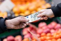 Ein Kunde bezahlt seinen Einkauf an einem Stand auf einem Wochenmarkt mit einem Fünf-Euro-Schein.