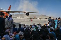 Afghan people sit as they wait to leave the Kabul airport in Kabul on August 16, 2021, after a stunningly swift end to Afghanistan's 20-year war, as thousands of people mobbed the city's airport trying to flee the group's feared hardline brand of Islamist rule. (Photo by Wakil Kohsar / AFP)