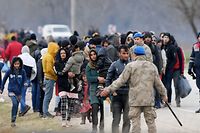 Migrants wait next Turkish soldiers as they resumed efforts to enter Europe next to the fences near Pazarkule border gate in Edirne on March 4, 2020. - Migrants and refugees clashed with Greek police on the Turkish border on March 4, 2020, as they resumed efforts to enter Europe, leaving at least one person injured according to AFP correspondents. (Photo by Ozan KOSE / AFP)