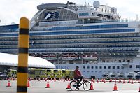 A man cycles past city buses (back L) lined up to transport the first batch of passengers disembarking from the Diamond Princess cruise ship - in quarantine due to fears of the new COVID-19 coronavirus - at the Daikoku Pier Cruise Terminal in Yokohama on February 19, 2020. - Relieved passengers began leaving a coronavirus-wracked cruise ship in Japan on February 19 after testing negative for the disease that has now claimed more than 2,000 lives in China. (Photo by CHARLY TRIBALLEAU / AFP)