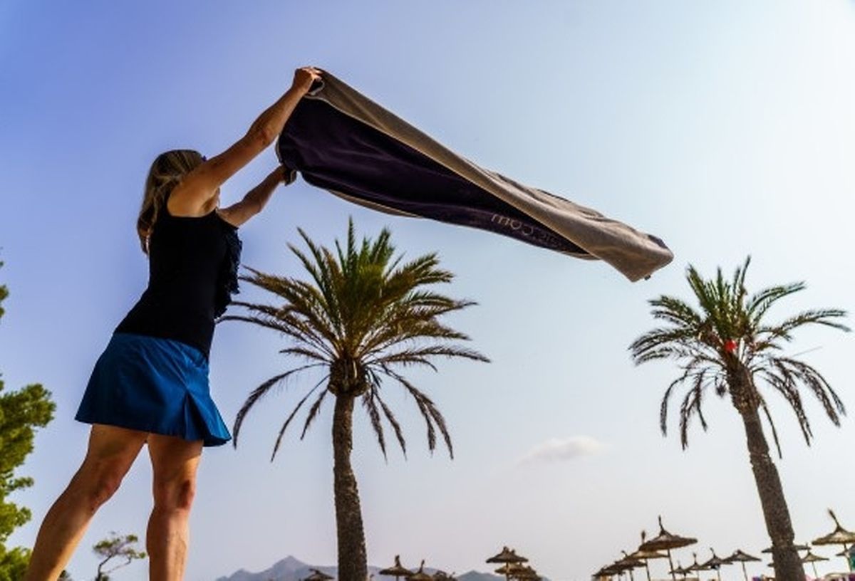 Eine Frau breitet am Strand von Alcudia ihr Handtuch aus - ein beliebter Frühsport in den Hotels.