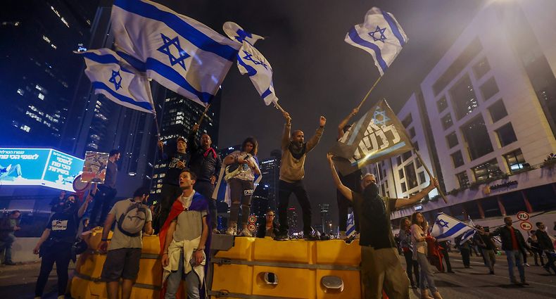 Israeli protesters wave national flags on a barricade as they block a road during a rally against the government's controversial judicial overhaul bill in Tel Aviv, on March 25, 2023. (Photo by AHMAD GHARABLI / AFP)