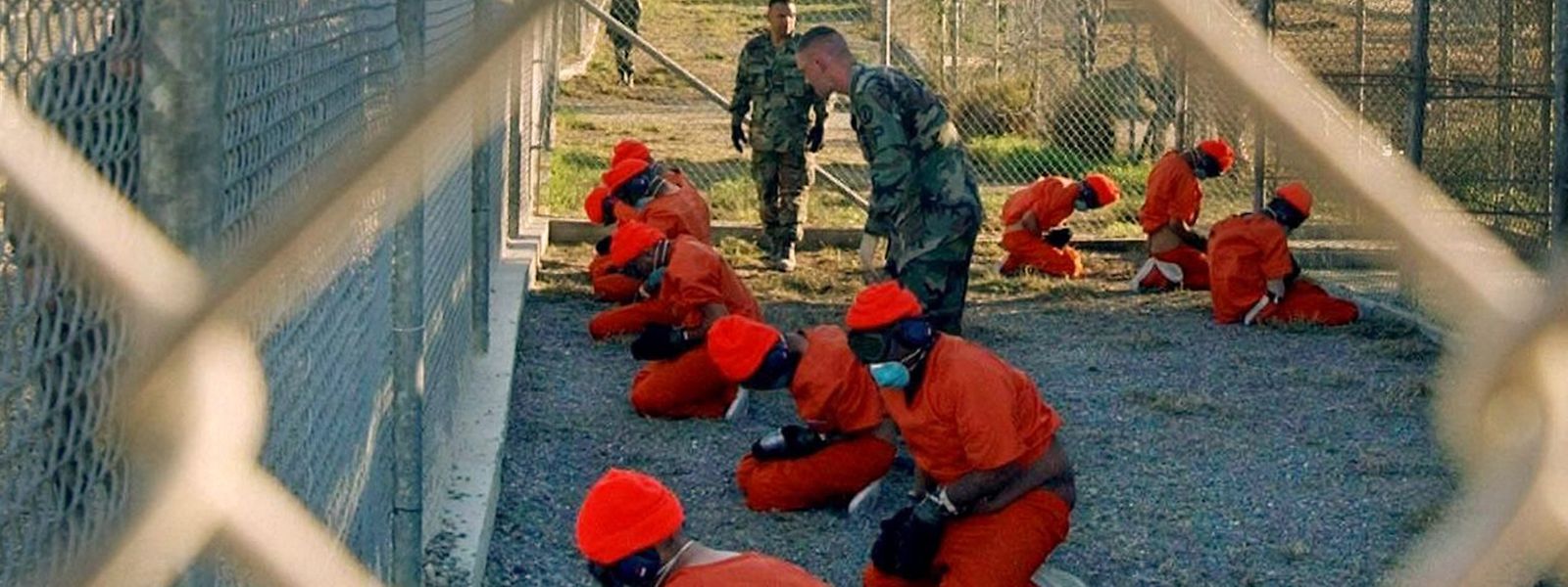 In orangefarbene Overalls gekleidete Häftlinge knien im US-Gefangenenlager Guantánamo.