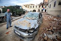 A man stands next to his damaged car and damaged buildings in Petrinja, some 50kms from Zagreb, after the town was hit by an earthquake of the magnitude of 6,4 on December 29, 2020. - The tremor, one of the strongest to rock Croatia in recent years, collapsed rooftops in Petrinja, home to some 20,000 people, and left the streets strewn with bricks and other debris. Rescue workers and the army were deployed to search for trapped residents, as a girl was reported dead. (Photo by Damir SENCAR / AFP)