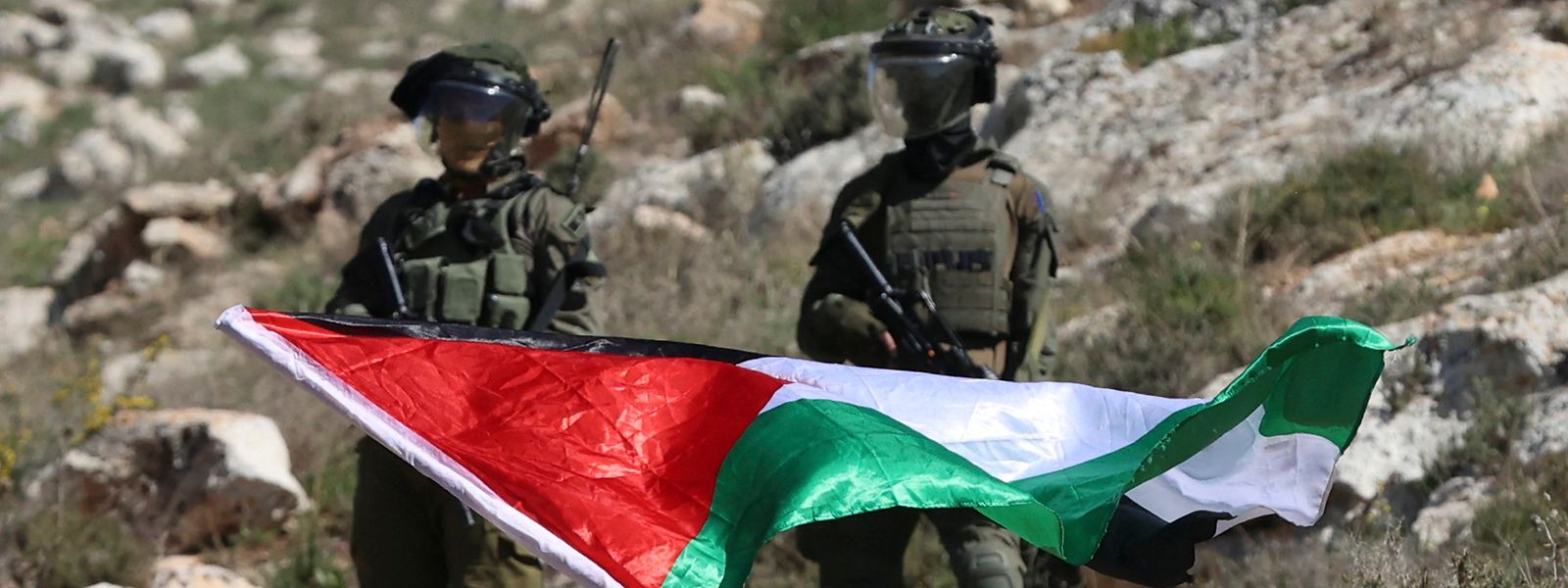 Ein palestinensischer Demonstrant schwingt unter Beobachtung zweier israelischer Soldaten die Nationalflagge. Damit protestiert er gegen die Errichtung von israelischen Außenposten nahe der West Bank-Stadt Nablus.