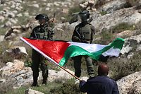 A Palestinian demonstrator facing Israeli troops waves a national flag  during a protest against the establishment of Israeli outposts, near the occupied-West Bank city of Nablus, on March 10, 2023. (Photo by Zain Jaafar / AFP)