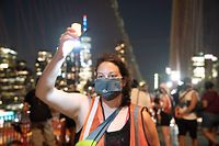 A woman holds up a candle as people participate in the "March for the Dead" across the Brooklyn Bridge, in memory of those who have died of COVID-19 and to protest the Trump administration's handling of the pandemic, on August 21, 2020 in New York. - The United States has recorded the most deaths with 174,290, according to Johns Hopkins University, followed by Brazil with 112,304, Mexico with 59,106, India with 54,849 and Britain with 41,403. (Photo by Bryan R. Smith / AFP)
