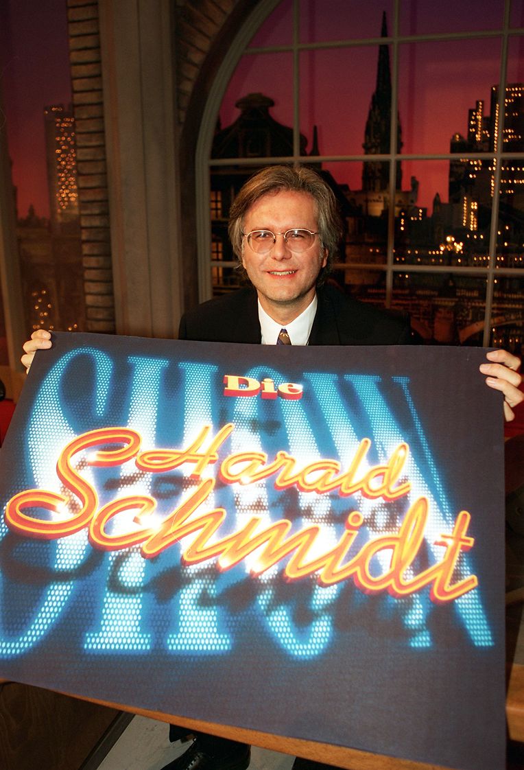 Der Moderator  präsentiert vor den Kulissen seiner neuen Show ein Schild mit der Aufschrift „Die Harald Schmidt Show“. 