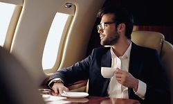 Smiling businessman holding cup and looking at window in private plane