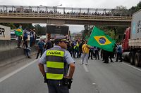 A police officers stands guard as supporters of President Jair Bolsonaro block Castelo Branco highway, on the outskirts of Sao Paulo, Brazil, on November 1, 2022. - Supporters of Brazilian President Jair Bolsonaro blocked major highways for a second day as tensions mounted over his silence after narrowly losing re-election to bitter rival Luiz Inacio Lula da Silva. Federal Highway Police (PRF) on Tuesday reported more than 250 total or partial road blockages in at least 23 states by Bolsonaro supporters, while local media said protests outside the country's main international airport in Sao Paulo delayed passengers and led to several flights being cancelled. (Photo by Caio GUATELLI / AFP)