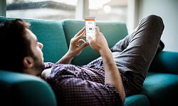 Close up of a young man lying on the bed and texting on his mobile phone