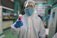TOPSHOT - A medical worker prepares to check the temperature of an AFP photojournalist before a COVID-19 coronavirus test in Wuhan in China's central Hubei province on April 16, 2020. - China has largely brought the coronavirus under control within its borders since the outbreak first emerged in the city of Wuhan late last year. (Photo by Hector RETAMAL / AFP)