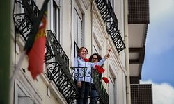 People hold up red carnations (symbol of the 25 April 1974 Portuguese Revolution) as they sing the Portuguese revolution anthem 'Grandola Vila Morena' marking 46th anniversary of 25th April Revolution at Graca neighborhood in Lisbon on April 25, 2020. - In the early morning of April 25, 1974, 'Grandola Vila Morena' by Portuguese singer-songwriter Zeca Afonso, was broadcasted on a Portuguese Catholic radio station, to signal the revolution kickoff, eventually becoming a symbol of the revolution and democracy in Portugal. The Portuguese celebrated the 46th anniversary of the Carnation Revolution today by singing at their windows, thereby circumventing the ban on gathering for traditional popular parades due to the coronavirus pandemic. (Photo by PATRICIA DE MELO MOREIRA / AFP)