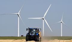 A farmer makes straw bales with his tractor after harvesting, on July 23, 2019, in Guigneville, centre France, in front of wind turbines. (Photo by Jean-Francois MONIER / AFP)