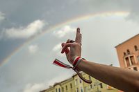 A person makes a V-sign wearing a bracelet with historical white-red-white colors of Belarus flag with a rainbow in the back as opposition supporters rally to protest against disputed presidential elections results in Minsk on August 27, 2020. (Photo by Sergei GAPON / AFP)