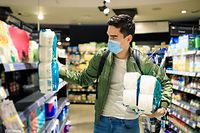 Panic buying toilet paper during Coronavirus. Young Man shopping in a supermarket, breathing through a medical mask because of the danger of getting the flu virus, influenza infection. Corona virus pandemic concept. Covid-19 virus!