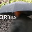 A man under an umbrella walks past the logo of the financial group Fortis NV near the entrance the company's headquarters in Brussels February 10, 2009. Fortis shareholders are due to meet on Wednesday in Brussels for a crucial vote over the break-up of the stricken group agreed last October -- involving the Netherlands' purchase of Fortis's Dutch activities, Belgium's purchase of the Belgian banking arm Fortis Bank, and BNP Paribas' acquisition of Belgian assets.  REUTERS/Thierry Roge   (BELGIUM)