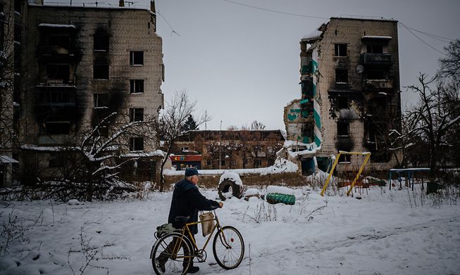 A resident pushes his bike next to destroyed residential buildings near Kyiv