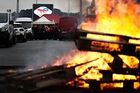 This photograph shows burning wood pallets as employees participate to a strike at the TotalEnergies raffinery site, in Gonfreville-l'Orcher, near Le Havre, northwestern France, on October 13, 2022. - TotalEnergies has eased up on salaries by announcing on October 13, 2022 an exceptional bonus equivalent to one month's salary for its employees worldwide, coupled with a proposed 6% increase in 2023 for French employees who have been on strike for 17 days in the refineries under threat of government requisition. The industrial action to demand pay hikes has paralysed six out of the seven fuel refineries in France, leading to shortages of petrol and diesel exacerbated by panic-buying from drivers. (Photo by Lou BENOIST / AFP)