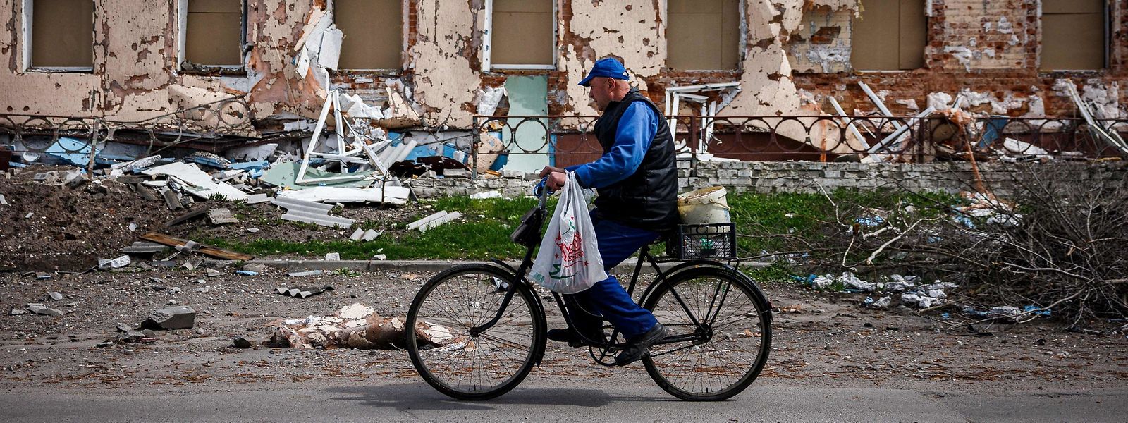 Im Dorf Derhachi nördlich von Charkiv radelt ein Mann mit seinen Einkäufen an einem zertrümmerten Gebäude vorbei.