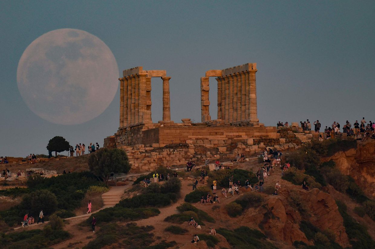Locais e turistas observam a Lua a nascer junto ao Templo de Poseidon no cabo de Sounion, cerca de 70 km a sul de Atenas