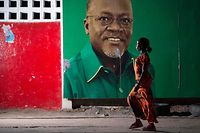 (FILES) In this file photo taken on October 29, 2015 A woman walks past an election billboard after ruling party Chama Cha Mapinduzi (CCM) candidate John Magufuli (pictured on the billboard) was named president-elect by the National Electoral Commission in Dar es Salaam. - Tanzanian President John Magufuli has died from a heart condition, his vice president said in an address on state television on March 17, 2021,, after days of uncertainty over his health and whereabouts. (Photo by Daniel Hayduk / AFP)