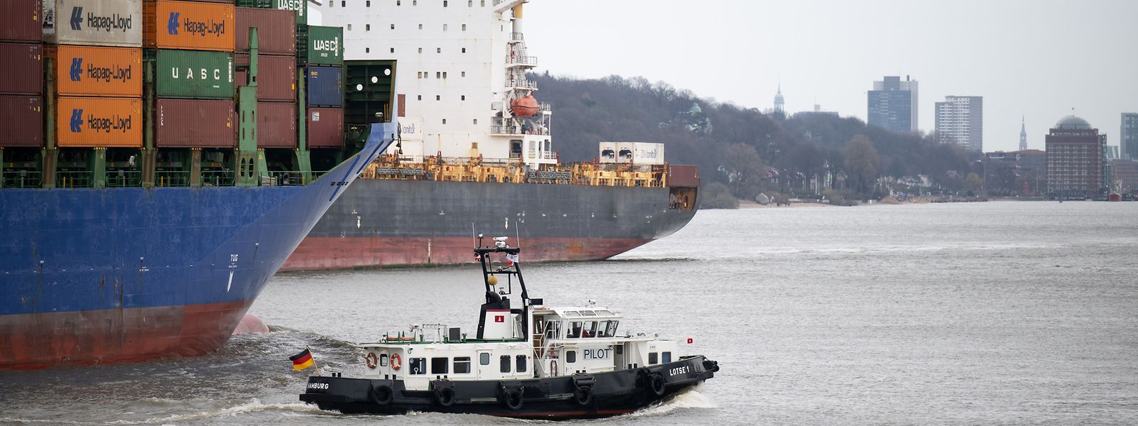 Ein Lotsenboot fährt neben einem Containerschiff in den Hamburger Hafen. Die HPA (Hamburg Port Authority) hat die Elbe für große Schiffe bereits gesperrt.