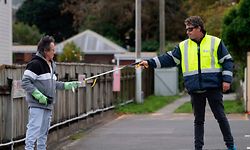 A man (L) is given an appointment slip by a security guard using a stick outside a COVID-19 coronavirus clinic in Lower Hutt, near Wellington, on April 20, 2020. - New Zealand will ease a nationwide COVID-19 lockdown next week after claiming success in stopping "an uncontrolled explosion" of the virus, Prime Minister Jacinda Ardern said on April 20. (Photo by Marty MELVILLE / AFP)