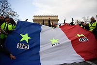Protestors wearing "yellow vests" (gilets jaunes) hold a French flag with yellow stars near the Arc de Triomphe in Paris on December 8, 2018 during a protest against rising costs of living they blame on high taxes. - Paris was on high alert on December 8 with major security measures in place ahead of fresh "yellow vest" protests which authorities fear could turn violent for a second weekend in a row. (Photo by Bertrand GUAY / AFP)