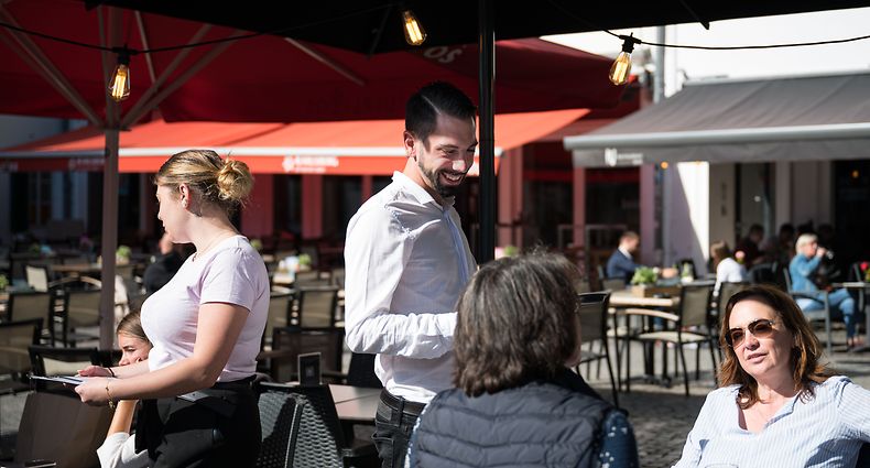 ARCHIV - 01.10.2021, Saarland, Saarbrücken: Eine Servicekraft des Restaurants iu in Saarbrücken bedient, ohne einen Mundschutz zu tragen, Kunden. Seit einer Woche sind die Corona-Regeln im Saarland drastisch gelockert. (zu dpa: «Corona-Lockerungen - Saarland genießt wieder Freiheiten») Foto: Oliver Dietze/dpa +++ dpa-Bildfunk +++