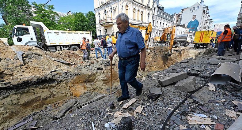 A pedestrian walks past communal employees working on a site of an overnight explosion in the centre of Kharkiv on June 6, 2023, following missile strike, amid the Russian invasion of Ukraine. (Photo by SERGEY BOBOK / AFP)