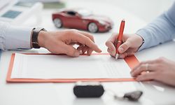 Woman signing a car insurance policy, the agent is pointing at the document