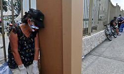A woman wearing a face mask mourns next to a cardboard box used as a coffin outside a cemetery in Guayaquyil, Ecuador, on April 6, 2020. - Soaring numbers of COVID-19 deaths in Ecuador's second city Guayaquil have led to a shortage of coffins, forcing locals to resort to using cardboard boxes, city authorities said Sunday. (Photo by Jose Sanchez / AFP)