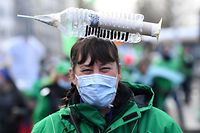 A health care worker carries a symbolic syringe shaped item on her head as she participates in a trade union demonstration against their mandatory anti-Covid 19 vaccination, as part of a major day of action, in Brussels on December 7, 2021. (Photo by JOHN THYS / AFP)