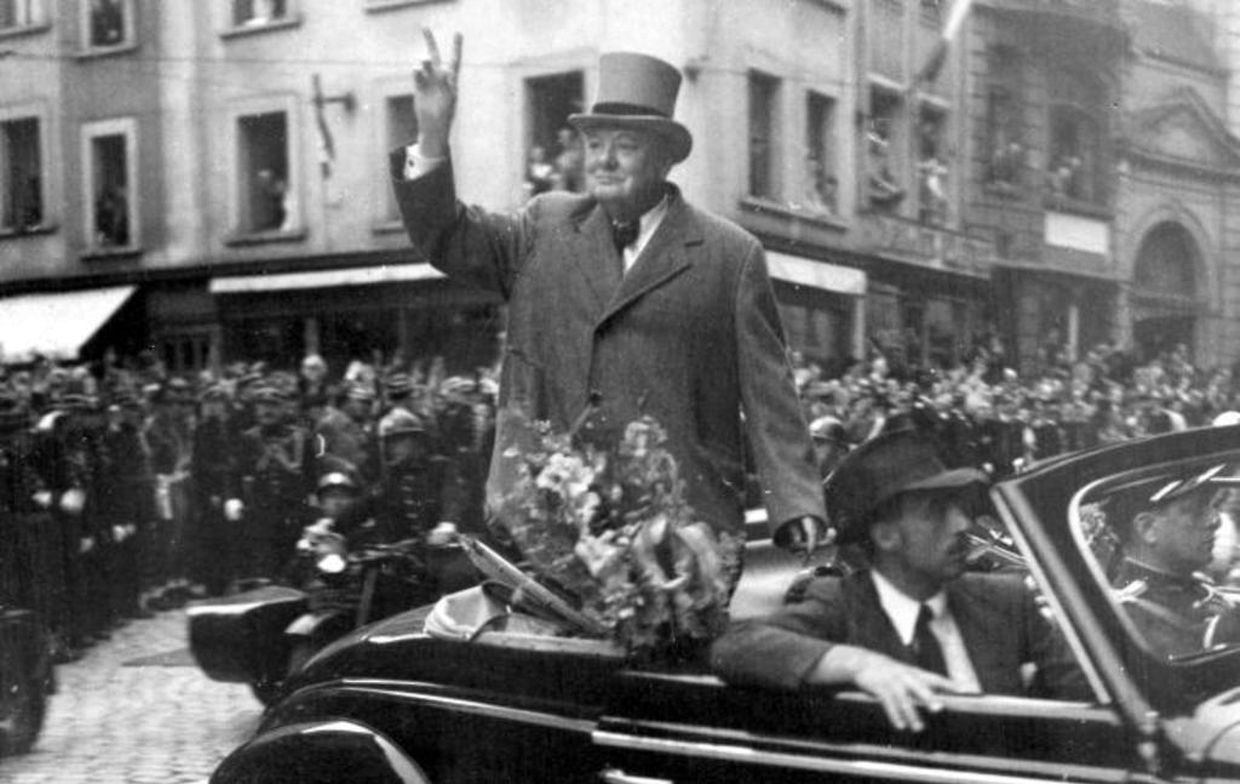 Churchill fährt, im Wagen stehend, die Zigarre rauchend und mit dem V-Zeichen grüßend, durch die von frenetischer Begeisterung widerhallenden Straßen der Stadt.