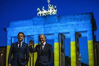 German Chancellor Olaf Scholz and French President Emmanuel Macron (L) wave as they visit the landmark Brandenburg Gate illuminated in the colors of the Ukrainian flag in Berlin on May 9, 2022, to show solidarity with Ukraine amid the ongoing Russian invasion. (Photo by John MACDOUGALL / AFP)