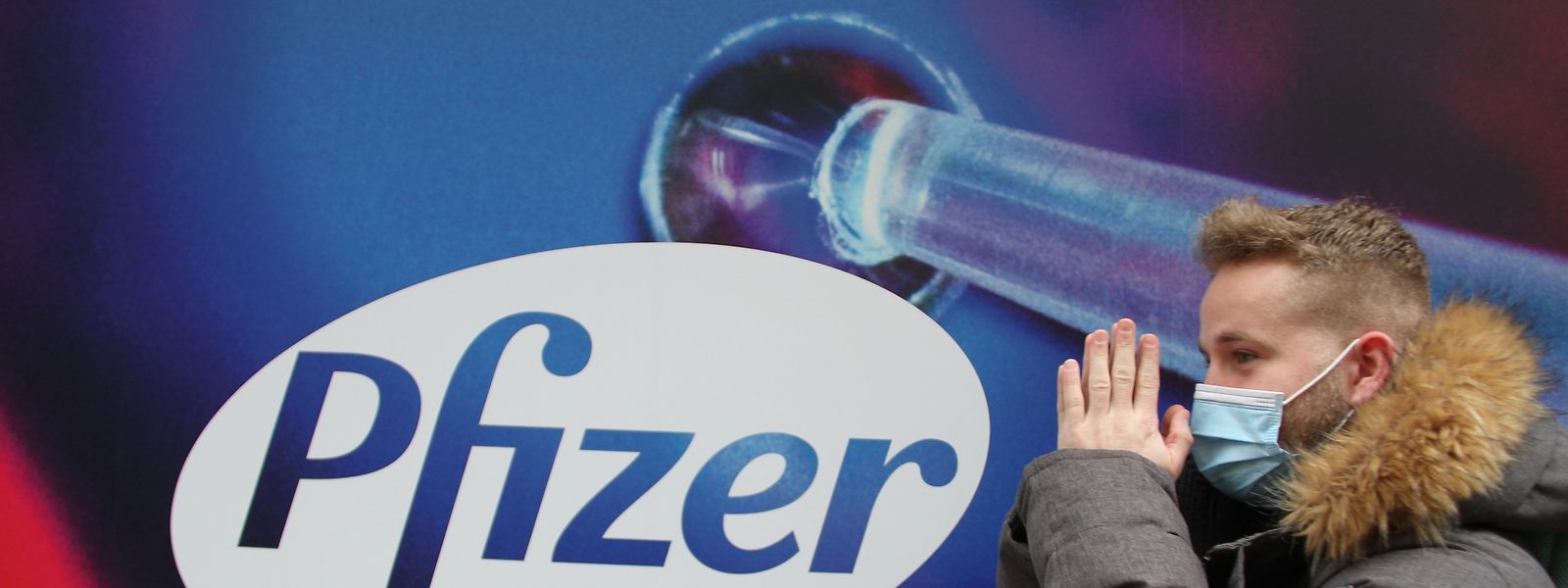 Um transeunte junto de um cartaz do fabricante de uma das vacinas contra a covid-19 que teve 'luz verde' para ser administrada nos EUA.