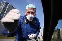 German doctor Michael Grosse takes a sample from a car driver through the window on March 27, 2020 at a drive through testing point for the novel coronavirus on a parking in Halle, eastern Germany. - German researchers plan to regularly test over 100,000 people to see if they have overcome infection with COVID-19 to track its spread, an institute behind the plan confirmed on March 27, 2020. (Photo by Ronny Hartmann / AFP)