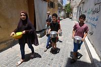 Crianças palestinianas levam tachos de comida para casa no campo de refugiados de Rafah, na Faixa de Gaza.