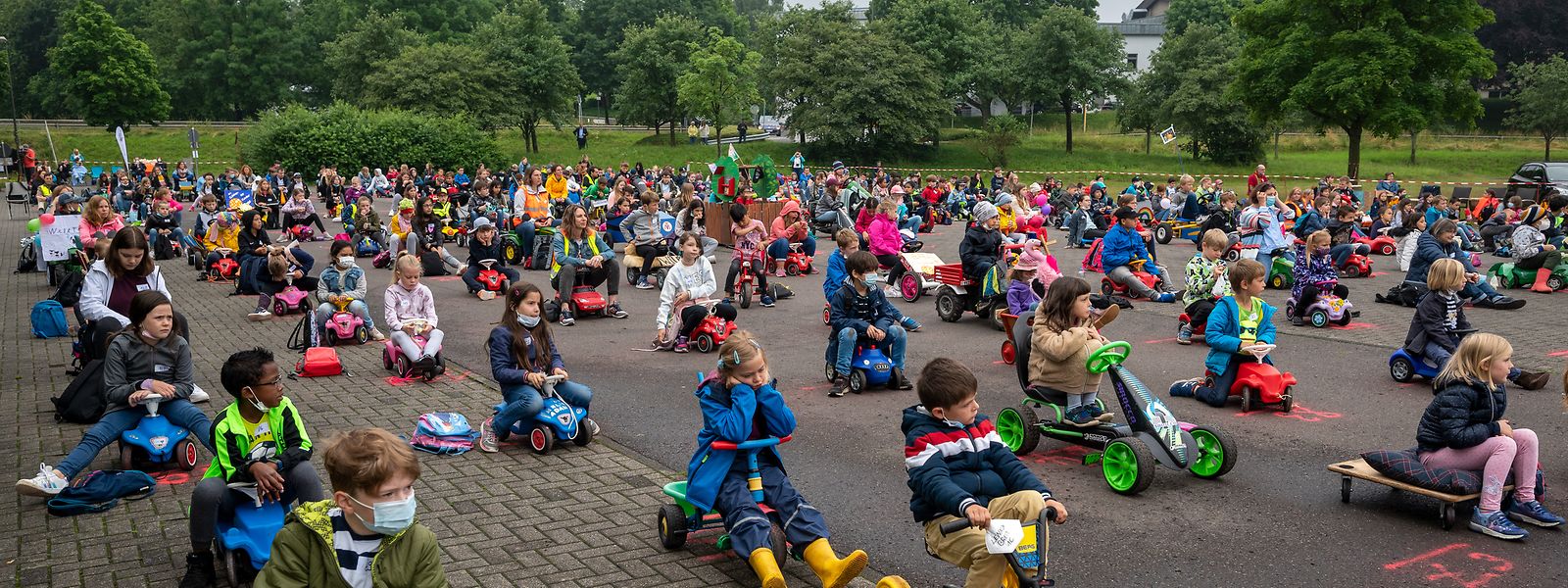 Kinder sitzen beim neuen Weltrekord im Vorlesen vor Kindern im Kinderfahrzeuge Drive-In in ihren unterschiedlichen Vehikeln. Kinder- und Jugendbuchautor Stefan Gemmel las dazu auf einem Parkplatz in Morbach aus einem seiner Bücher vor.